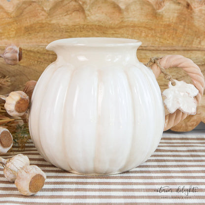 Functional ceramic white pumpkin pitcher ideal for serving drinks, showcased with mixed green foliage.